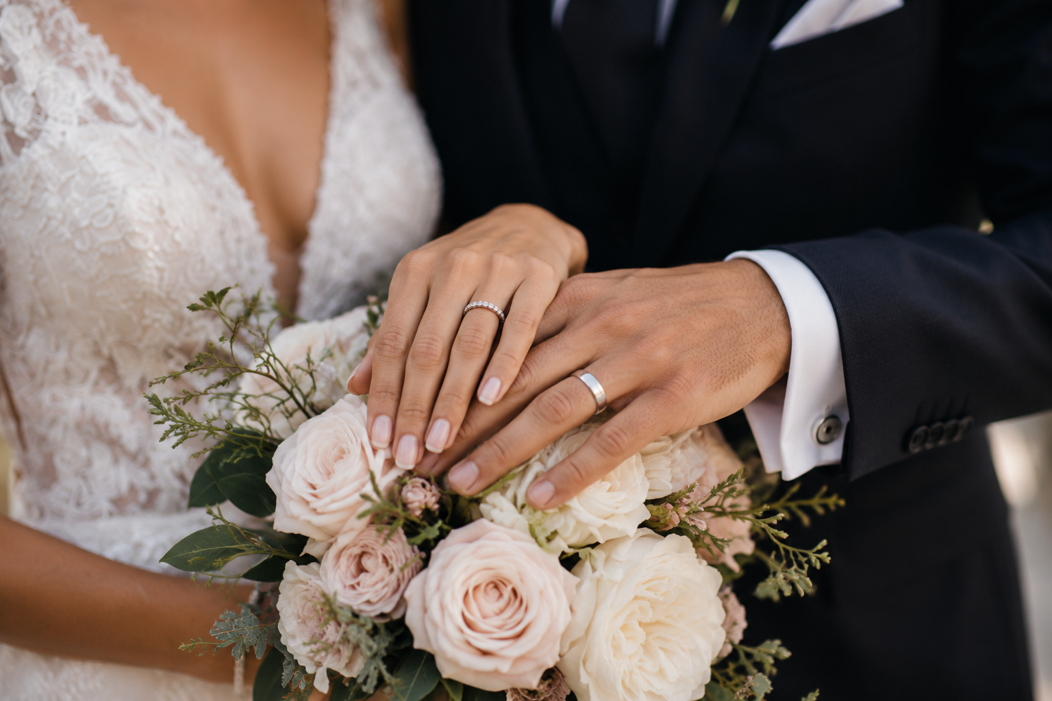 Detalle real de las manos de los novios y los anillos sobre el ramo